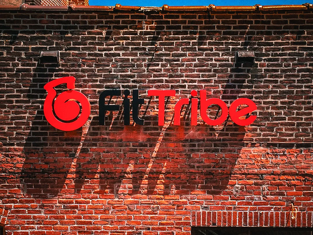 Commercial exterior sign for Fit Tribe on textured brick wall