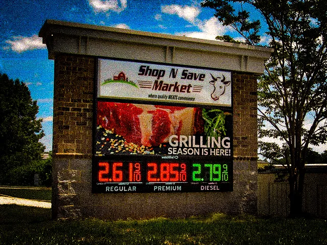 Commercial exterior sign with market logo, grilling promo, and fuel prices