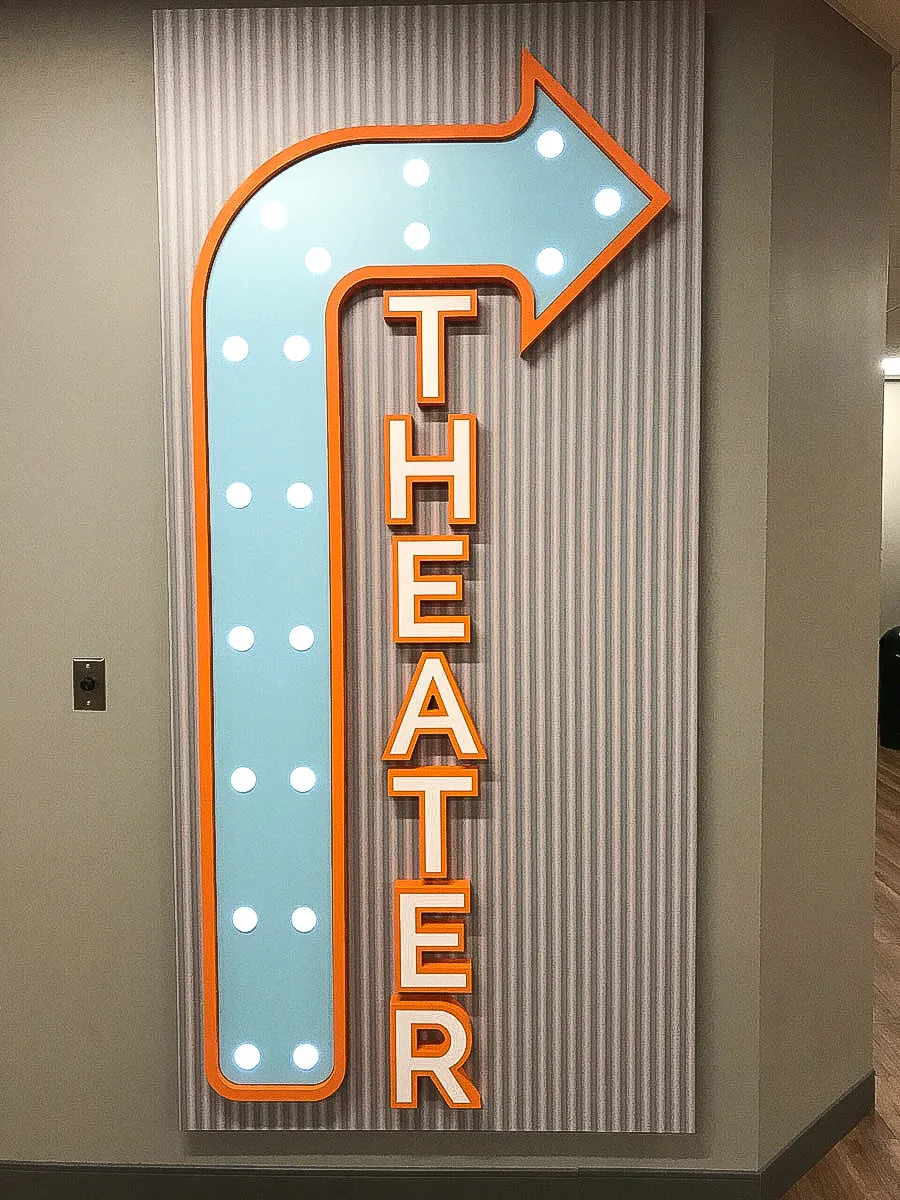 Commercial interior sign with illuminated arrow pointing to Theate