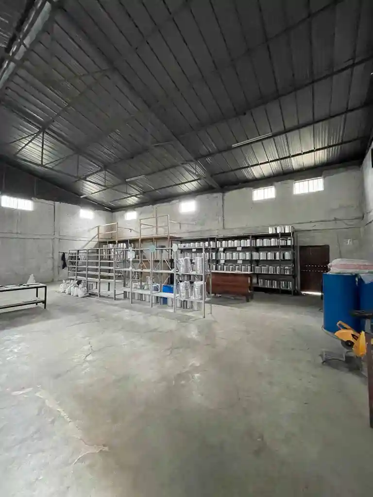 Spacious industrial warehouse with metal shelves holding metal containers and bags on the floor.