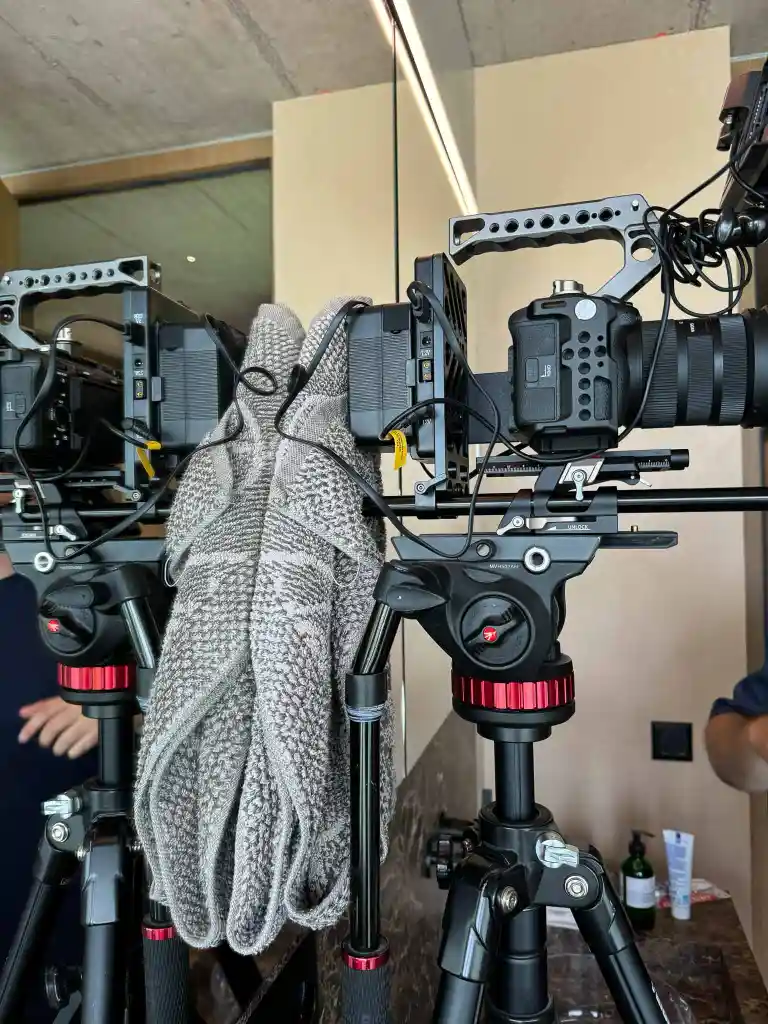 Professional camera mounted on a tripod with a gray knit sweater draped over the tripod, reflected in a mirror behind it.