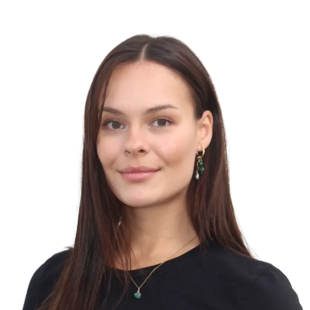 Portrait of a young woman with long brown hair wearing green stone earrings and a matching necklace, dressed in a black top.