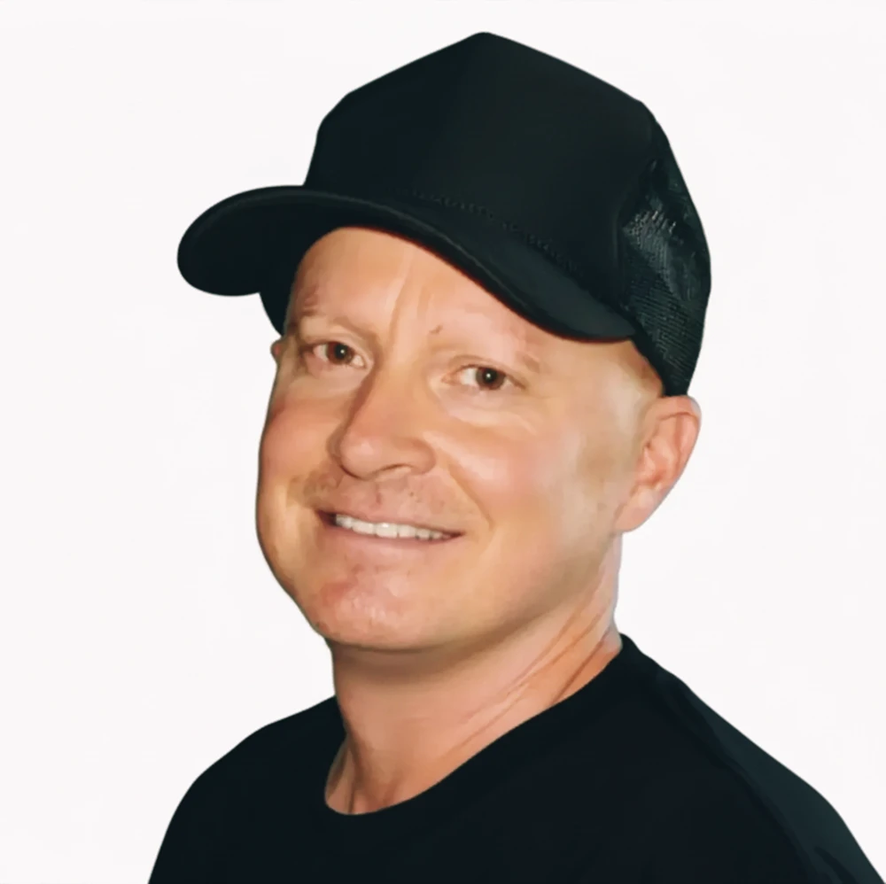 Smiling man wearing a black cap and black shirt against a white background.