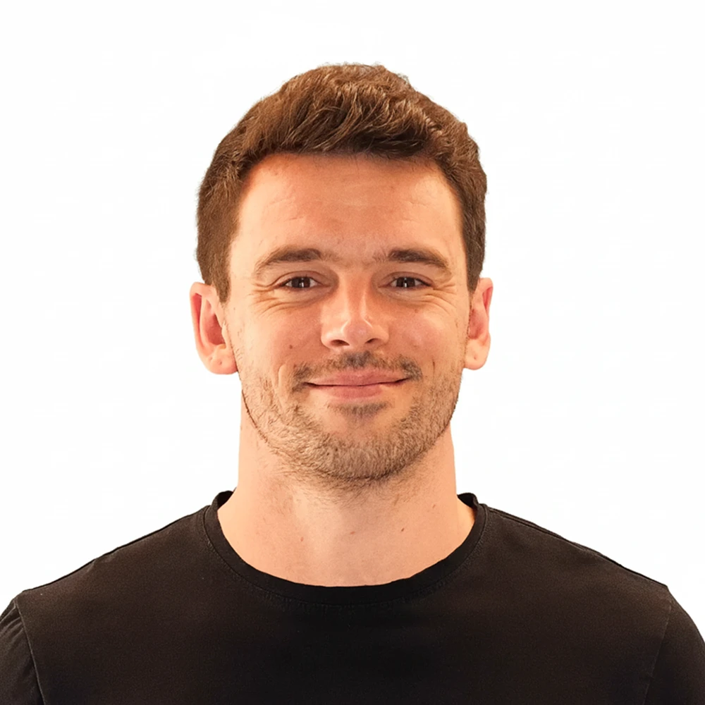 Smiling man with short brown hair, light beard, wearing a black t-shirt against a white background.