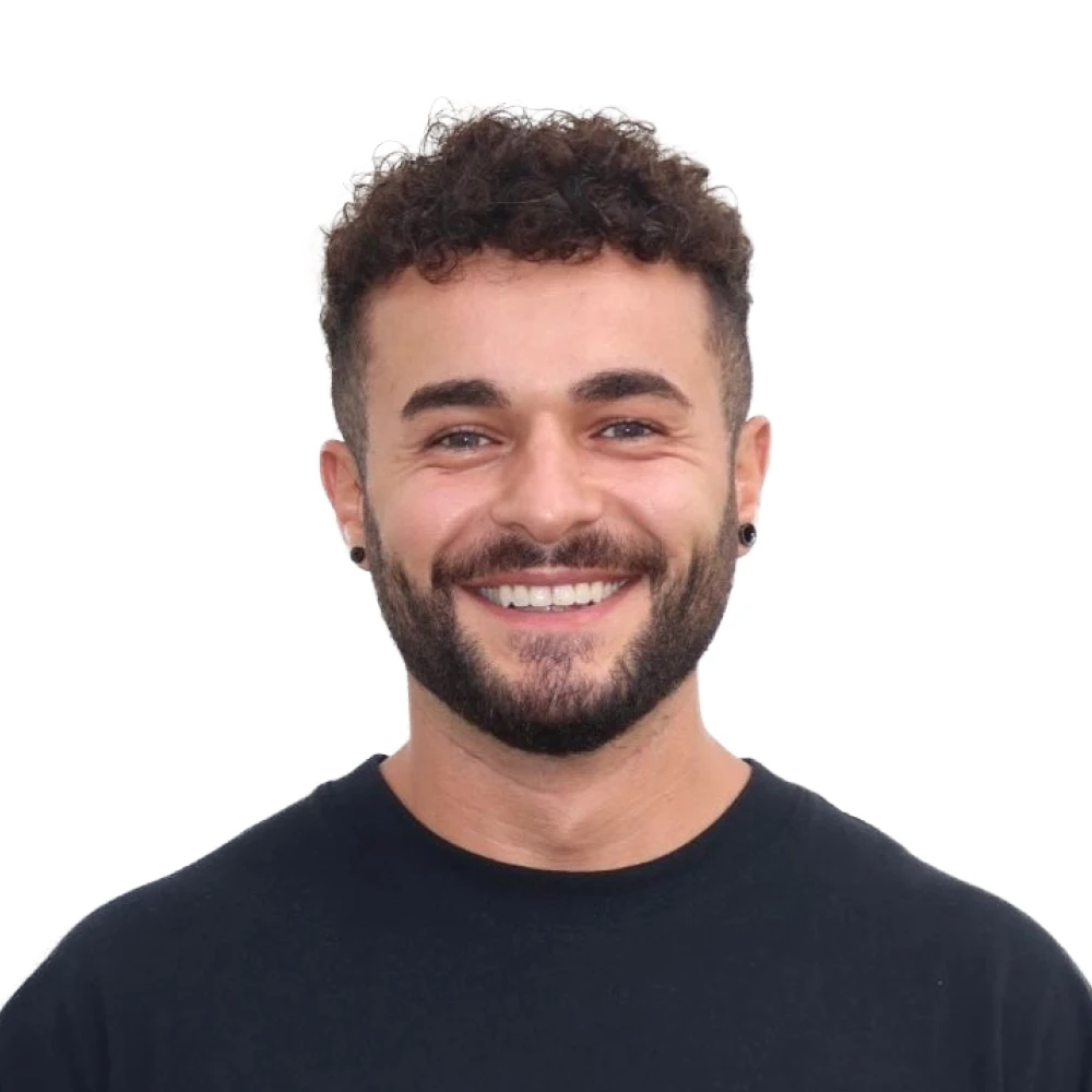 Smiling man with curly hair, beard, black earrings, and black shirt against a white background.