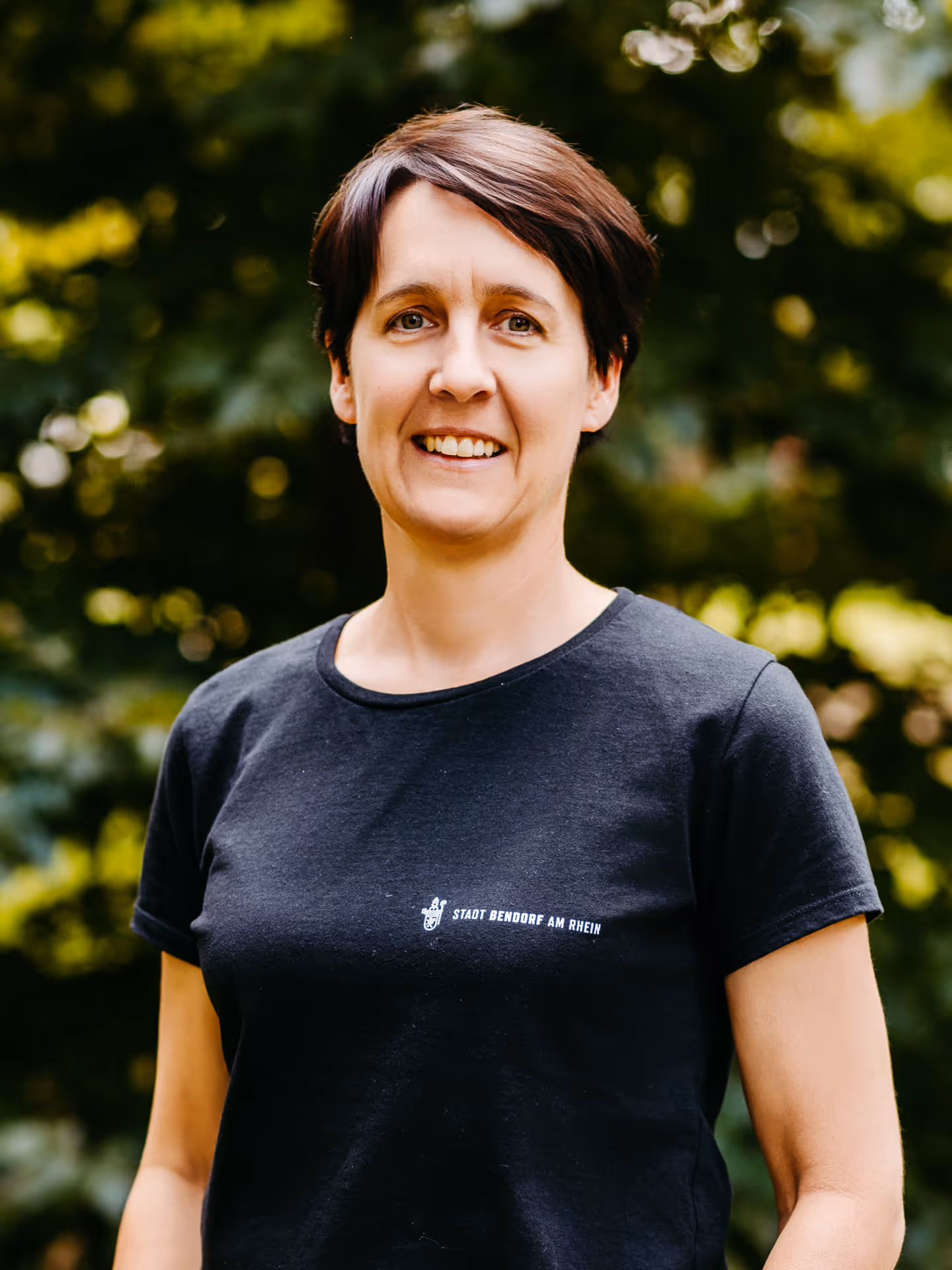 Ein lächelnde Frau mit dunklen Haaren und schwarzem T-Shirt mit der Aufschrift "Stadt Bendorf am Rhein"