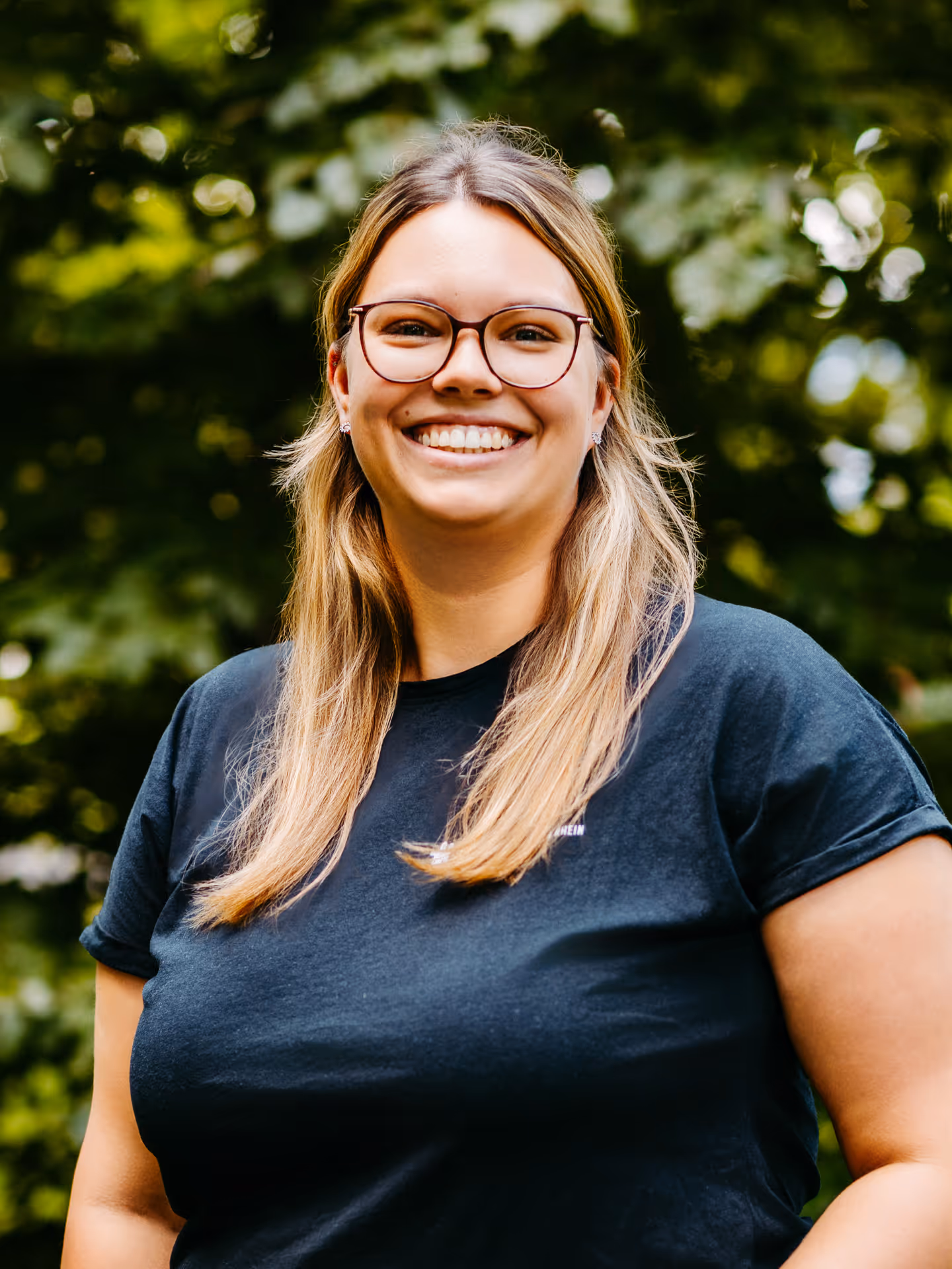 Eine lächelnde Frau mit blonden, schulterlangen Haaren, dunkler Brille und schwarzem T-Shirt mit der Aufschrift "Stadt Bendorf am Rhein"