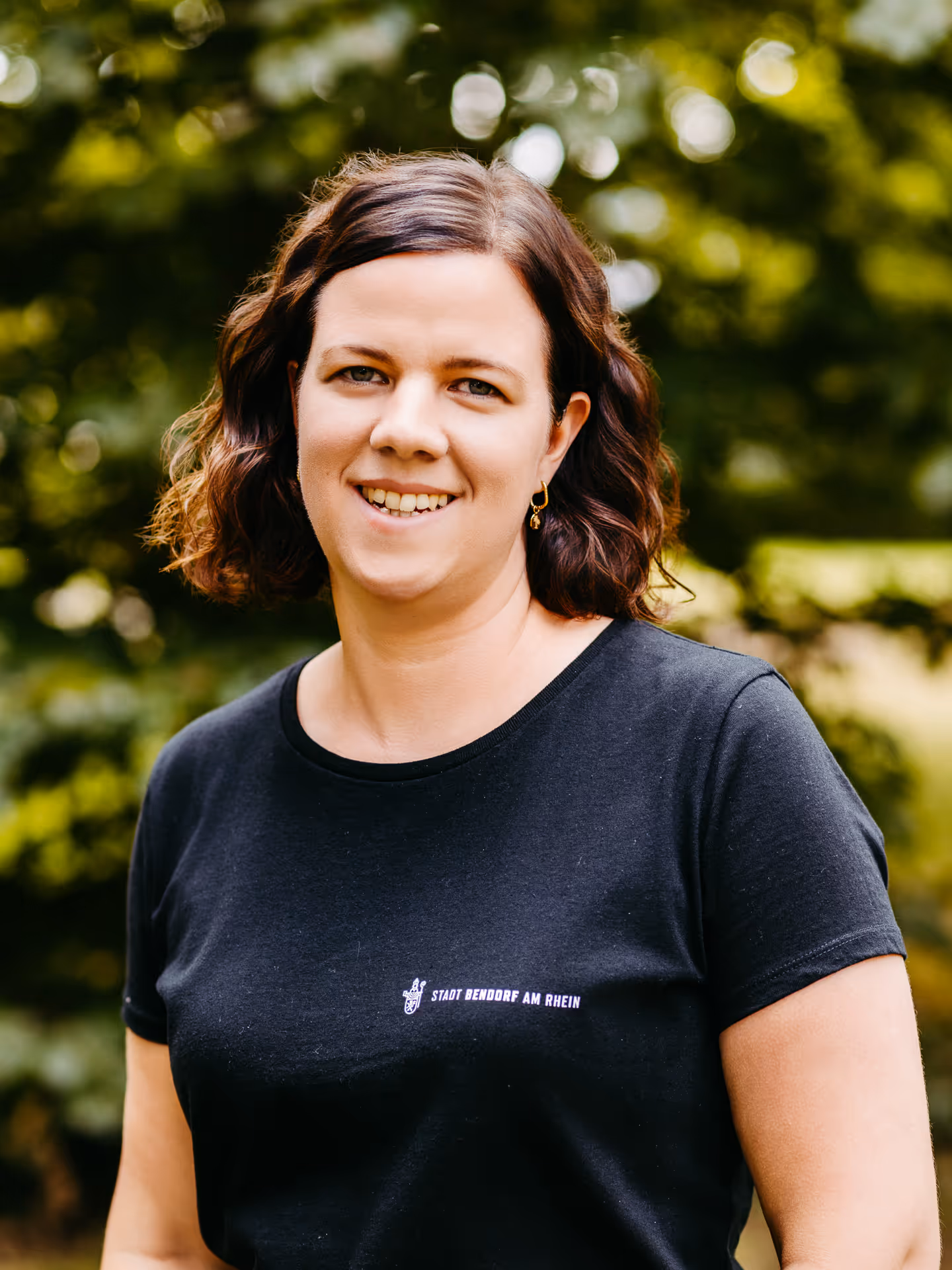 Eine lächelnde Frau mit dunkelbraunen Haaren und schwarzem T-Shirt mit der Aufschrift "Stadt Bendorf am Rhein"