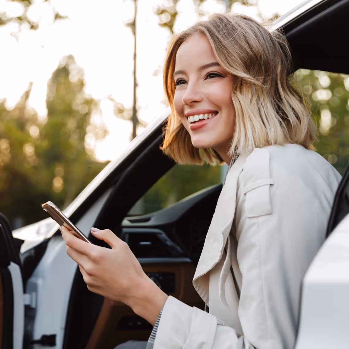 Mitarbeiterin steigt mit dem Smartphone in der Hand aus ihrem Dienstwagen