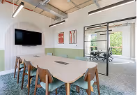 Modern, bright office meeting room with white table, chairs, and wall-mounted TV