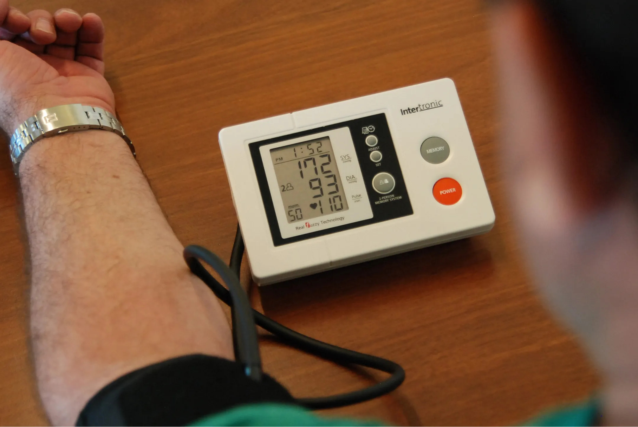 A person wearing a green shirt and black wristband holding a blood pressure monitor.