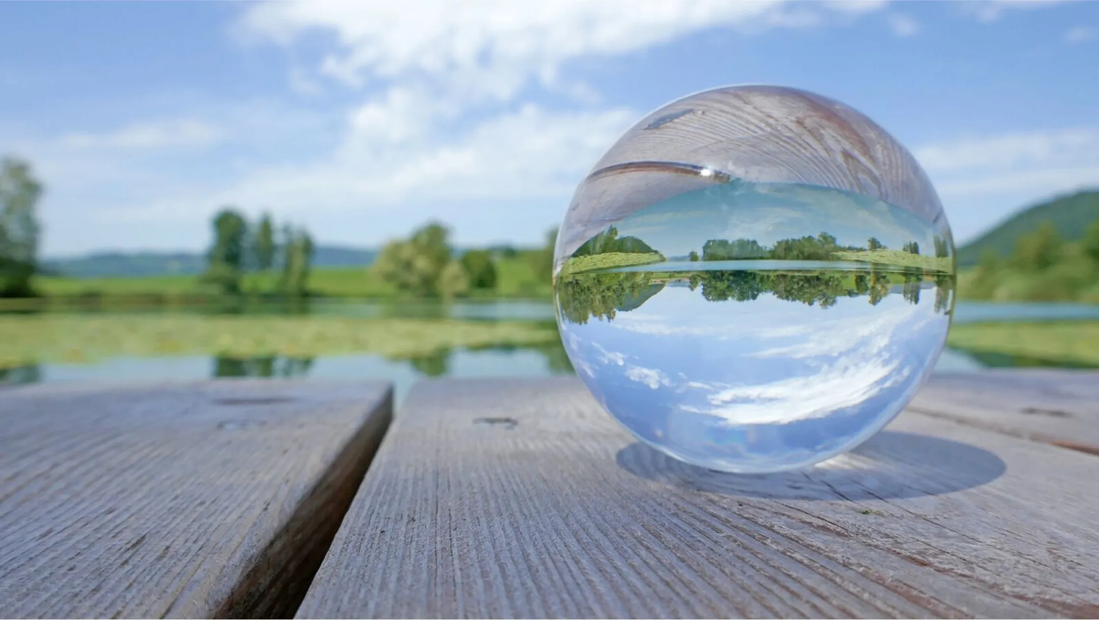 Eine Glaskugel mit der Spiegelung eines Baumes und Wassers.