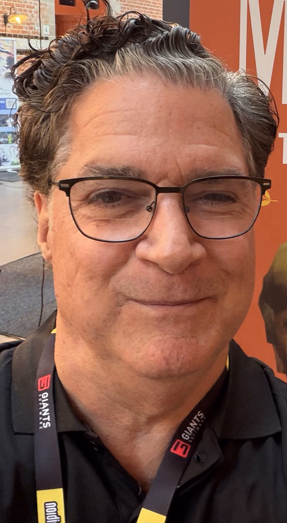 Middle-aged man with curly graying hair and glasses wearing a black shirt and lanyard.