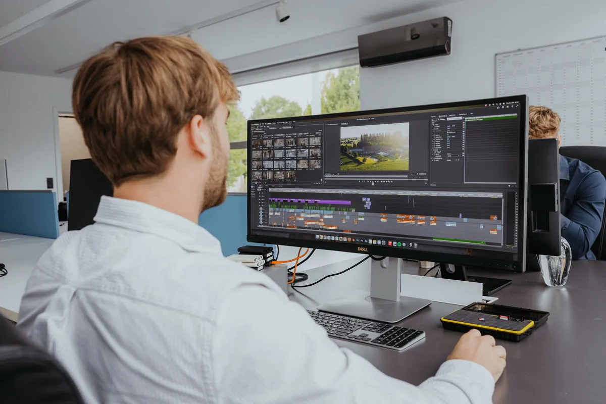 Man editing a video timeline on a large computer monitor in a modern office.