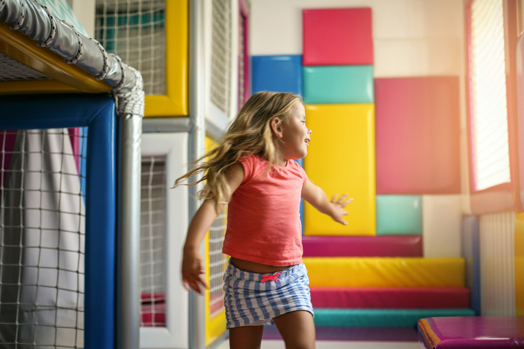 Young girl spinning with arms outstretched inside a colorful indoor play area.