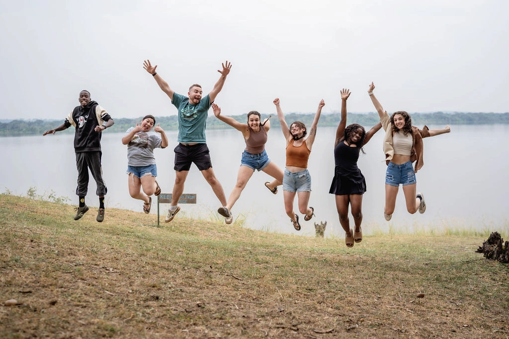 A group of young children and young adults jumping in the grounds of Murchison River lodge with the River Nile as a backdrop 