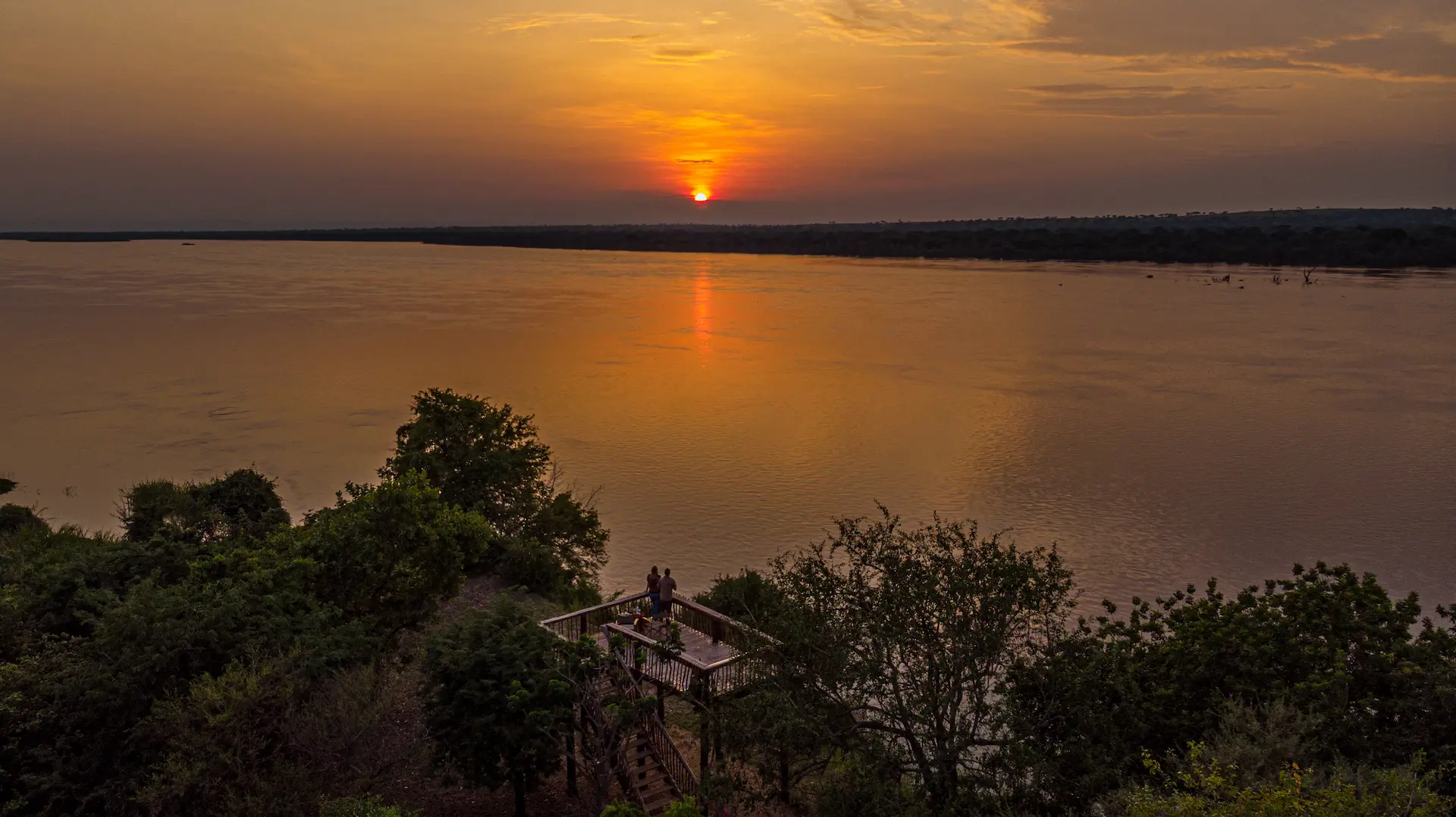 Guests on the viewing platform enjoying the sunset illuminating the sky over the River Nile and Murchison Falls National Park.