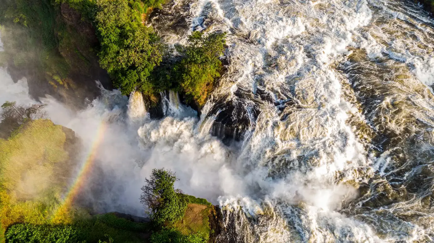 Drone close-up of the River Nile crashing through the gap of Murchison Falls with rainbow overhead.