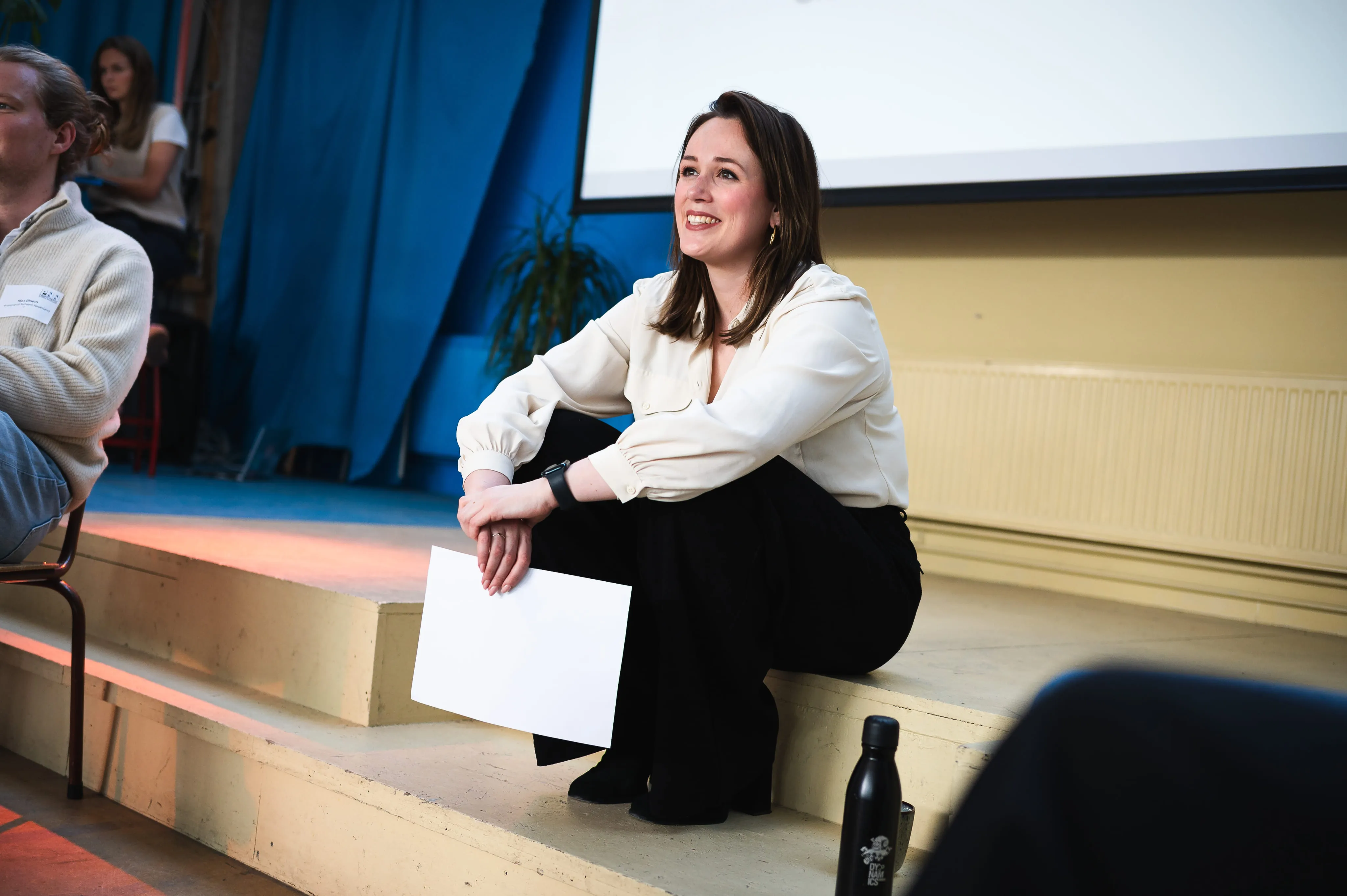 Woman smiling and sitting on stage, holding a document