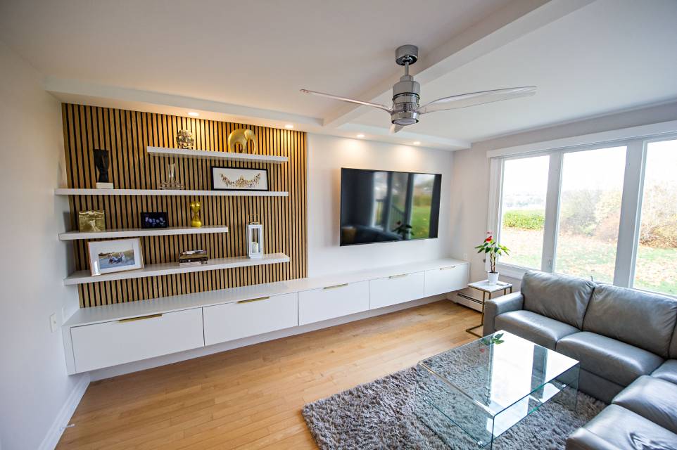 Bright family room with a slat-wood media wall, a ceiling fan, and large windows