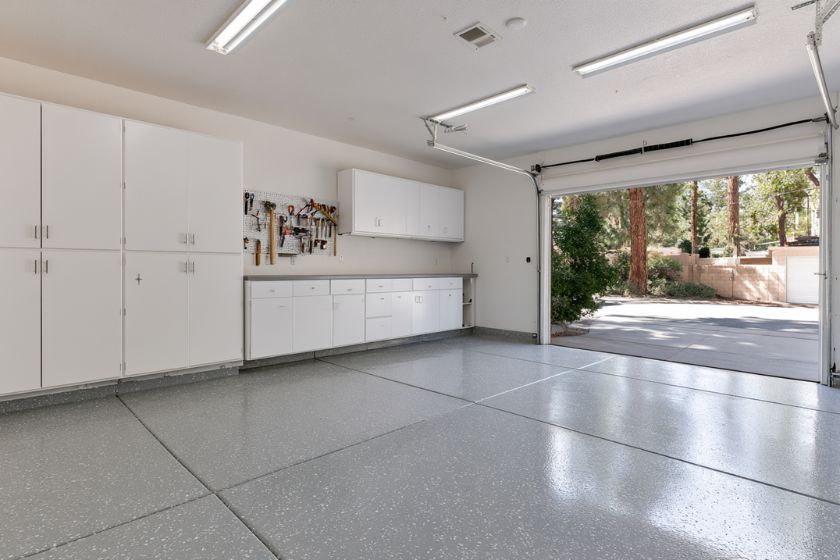 Interior of a garage before conversion, with an epoxy floor, built-in cabinets, and an open door to the yard