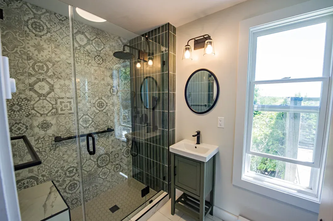 Dartmouth bathroom with patterned tile glass shower, green vanity and round mirror