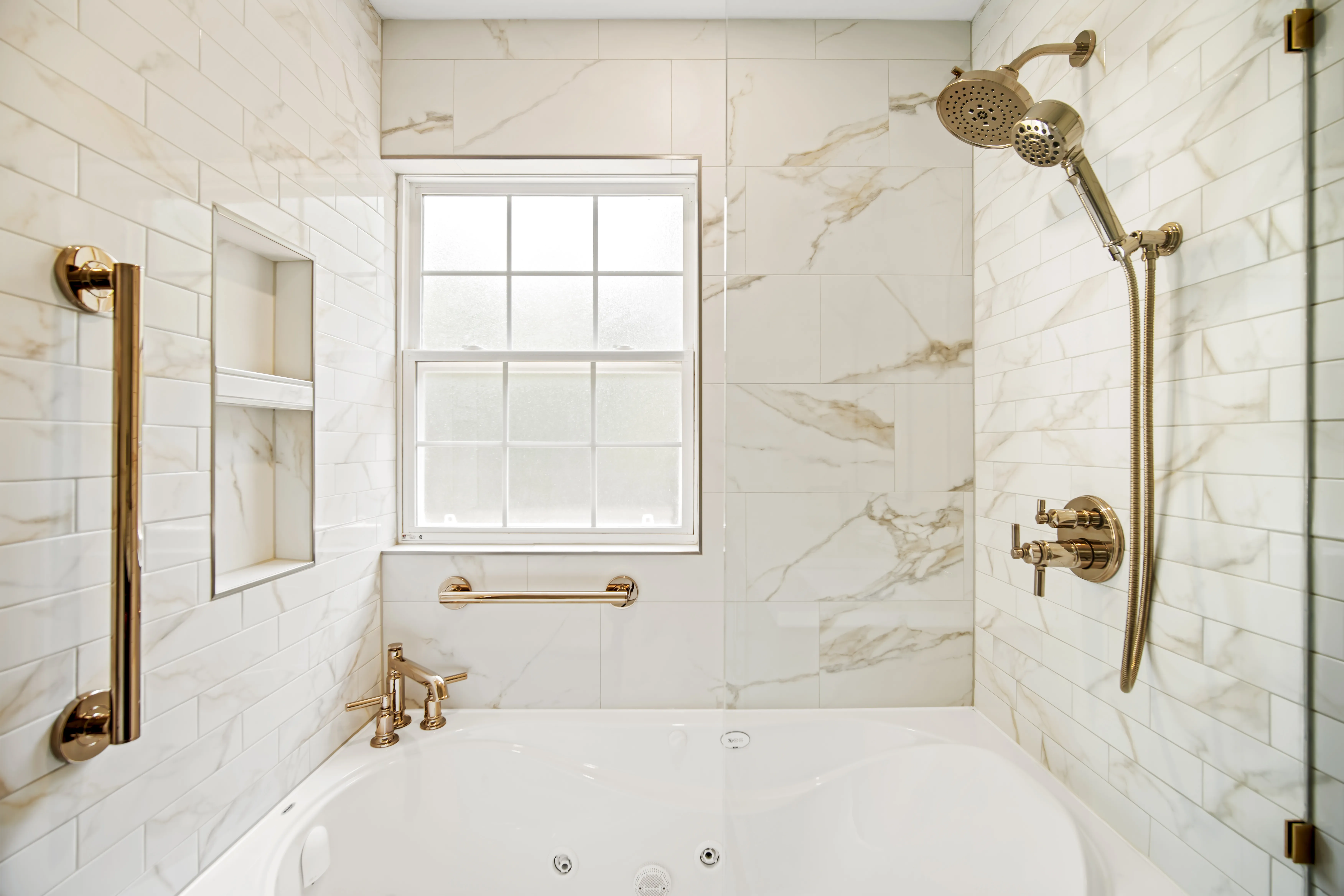 Tub and shower alcove with a brass rain head, a hand shower and a grab bar
