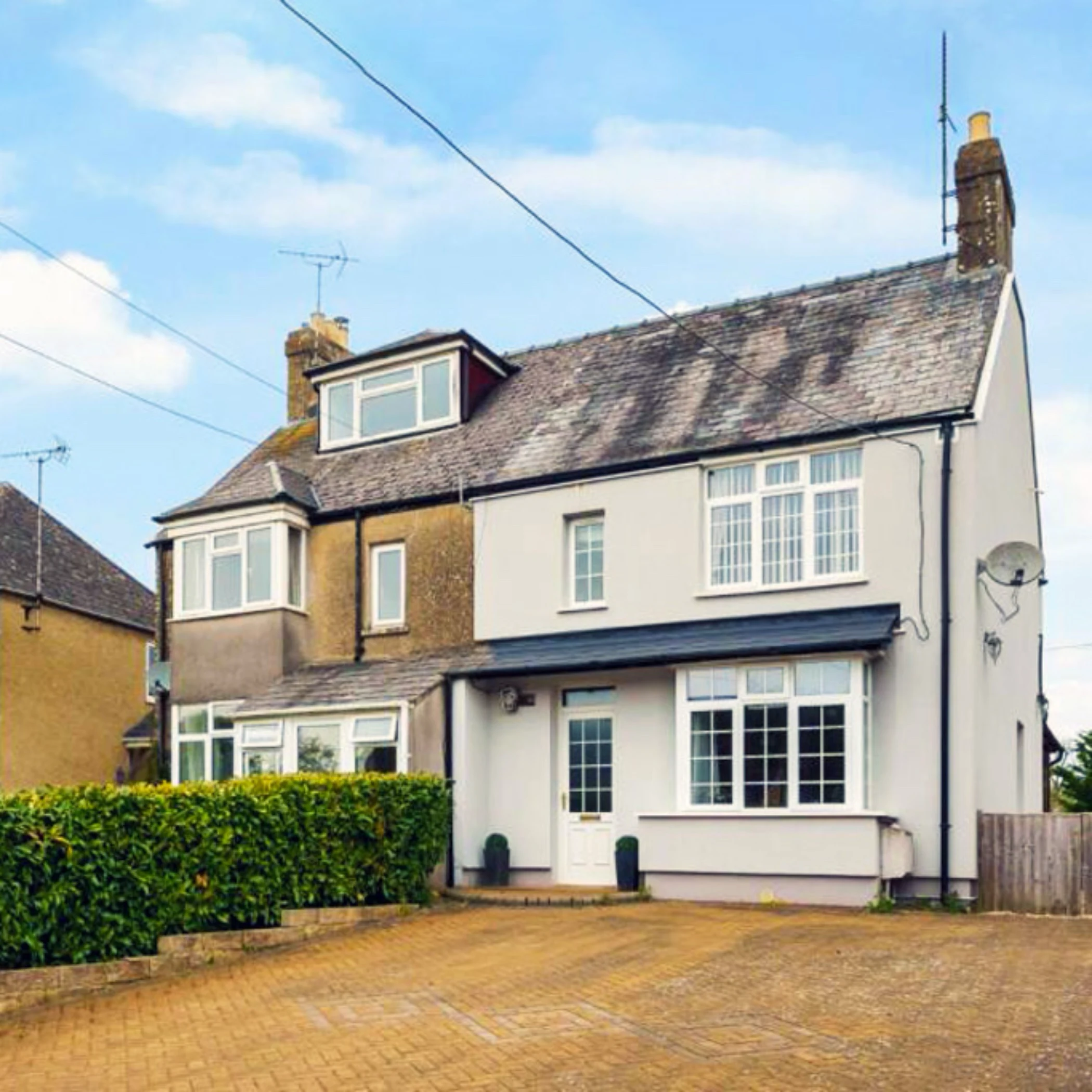 Semi-detached suburban home with a mixed exterior of pebbledash and smooth render. Features include a bay window, pitched roof with mossy patches, dormer loft extension, and a paved front driveway bordered by hedges.