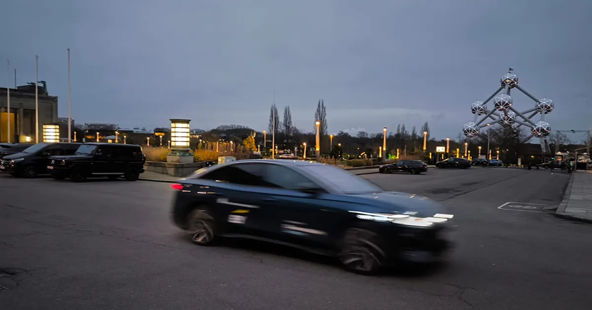 Blurred dark car speeding on a street at dusk with the Atomium structure visible in the background.
