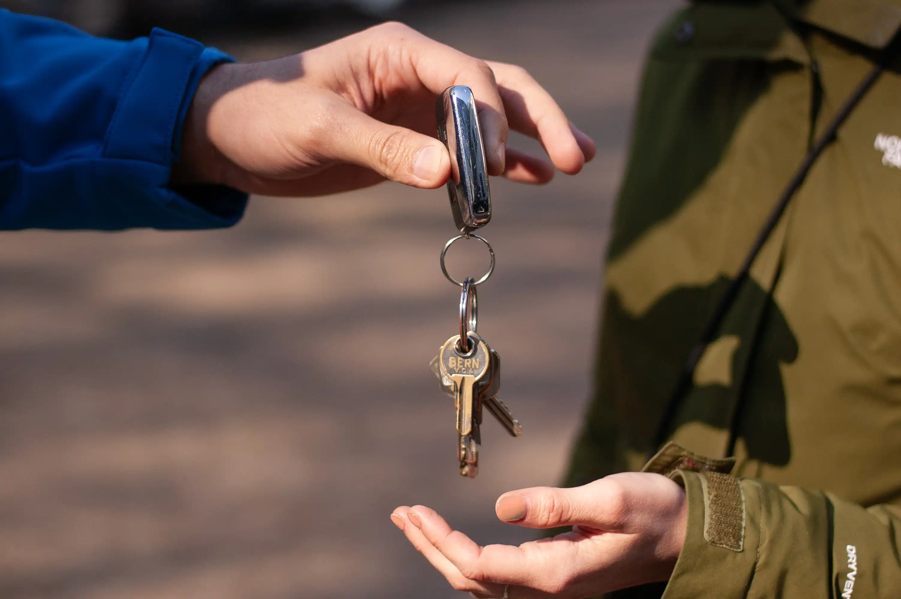 Person in a blue sleeve handing a set of keys to another person wearing a green jacket.