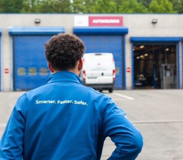 Person in blue jacket with 'Smarter. Faster. Safer.' on back facing a building with blue garage doors.