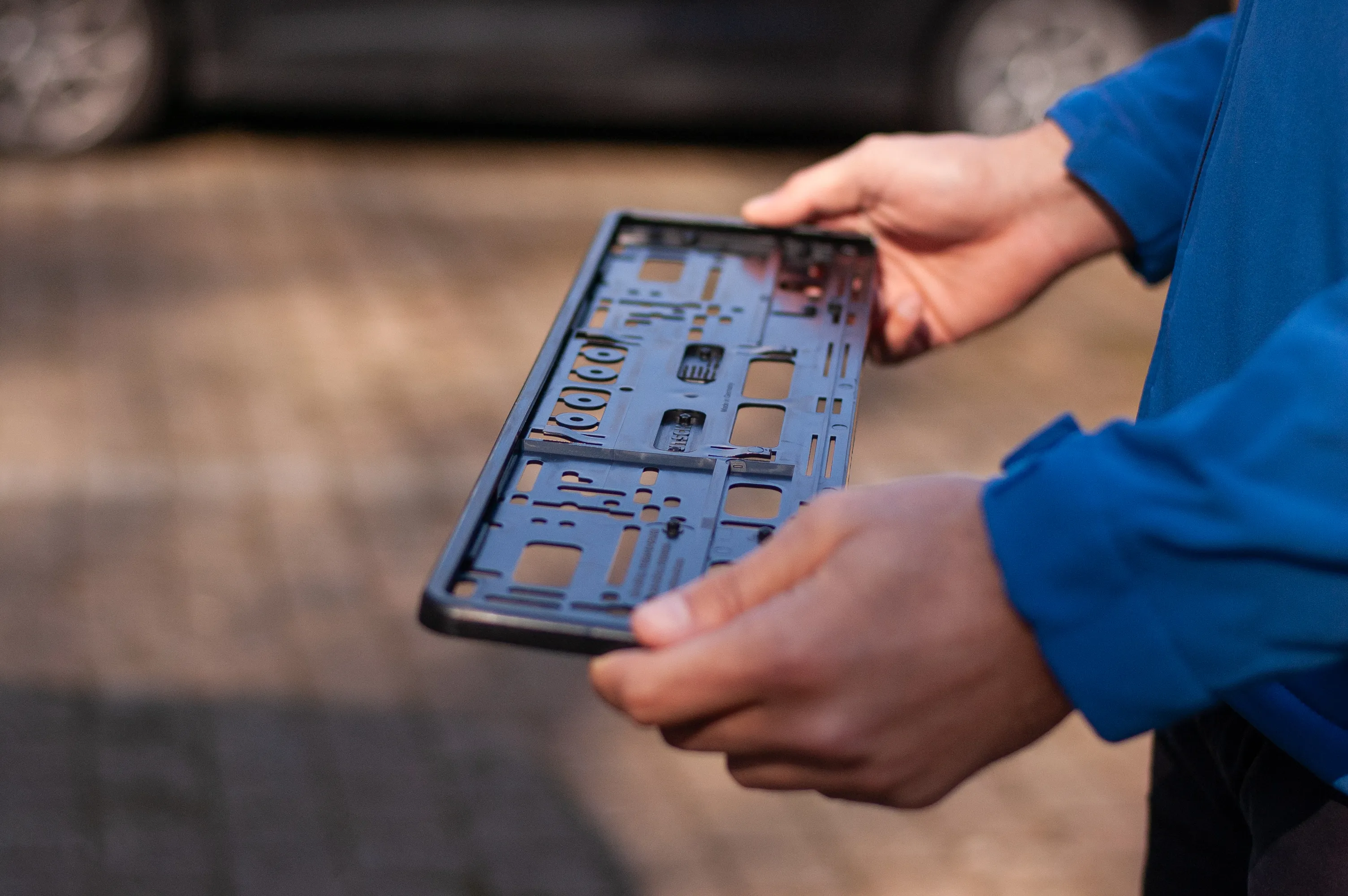 Person holding a black car license plate holder outdoors with blurred background.