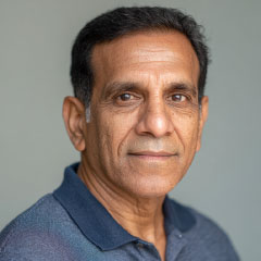 Headshot of an Indian man wearing a dark collared shirt, looking directly at the camera. Neutral background with a calm and composed expression.