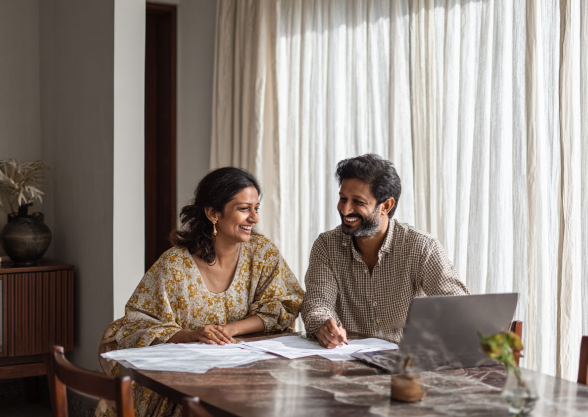 indian couple smiling at each other with financial papers in front of them