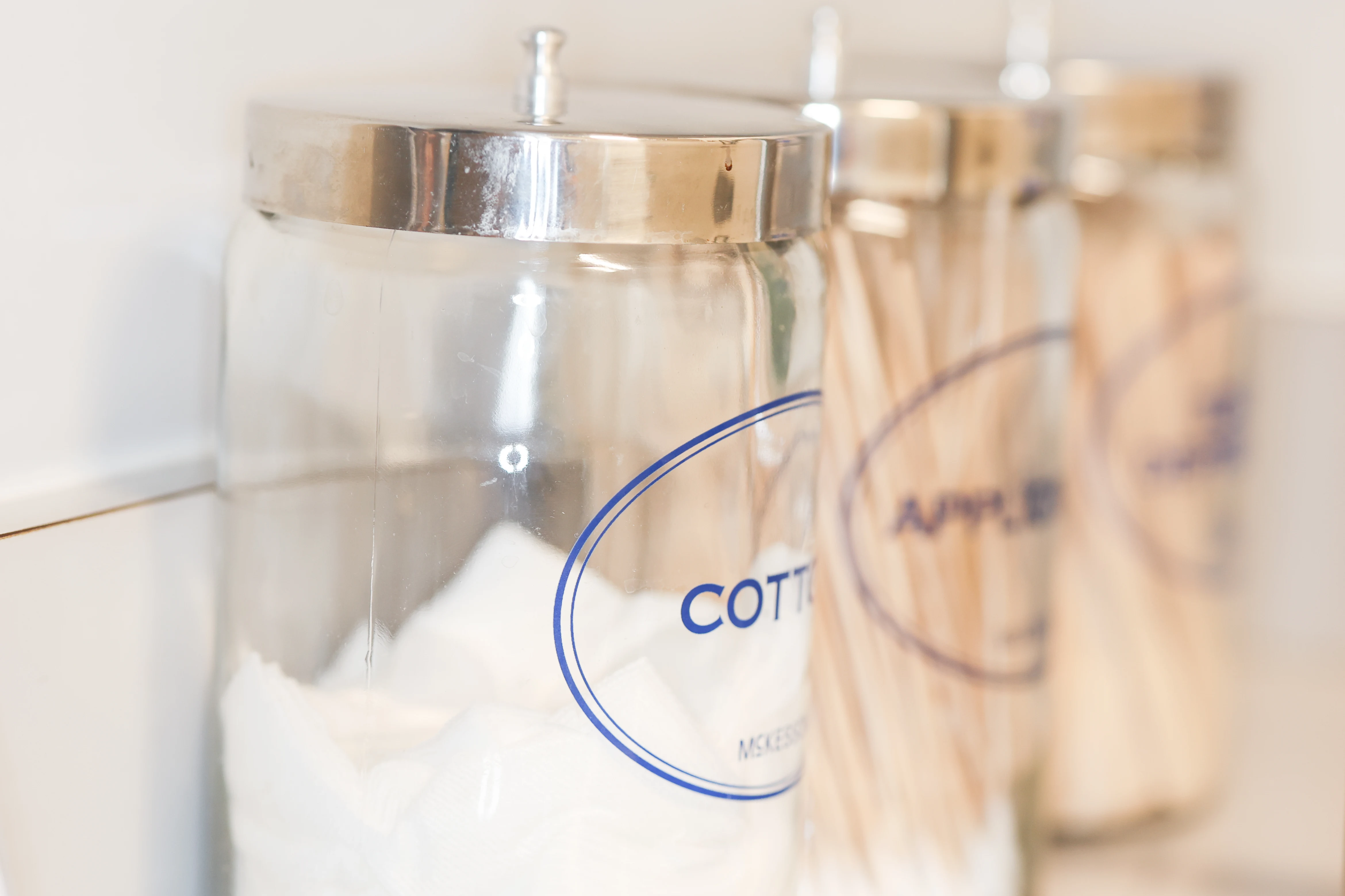 Close-up of glass jars labeled cotton and applicators, showcasing neat, hygienic storage of medical supplies in exam room.
