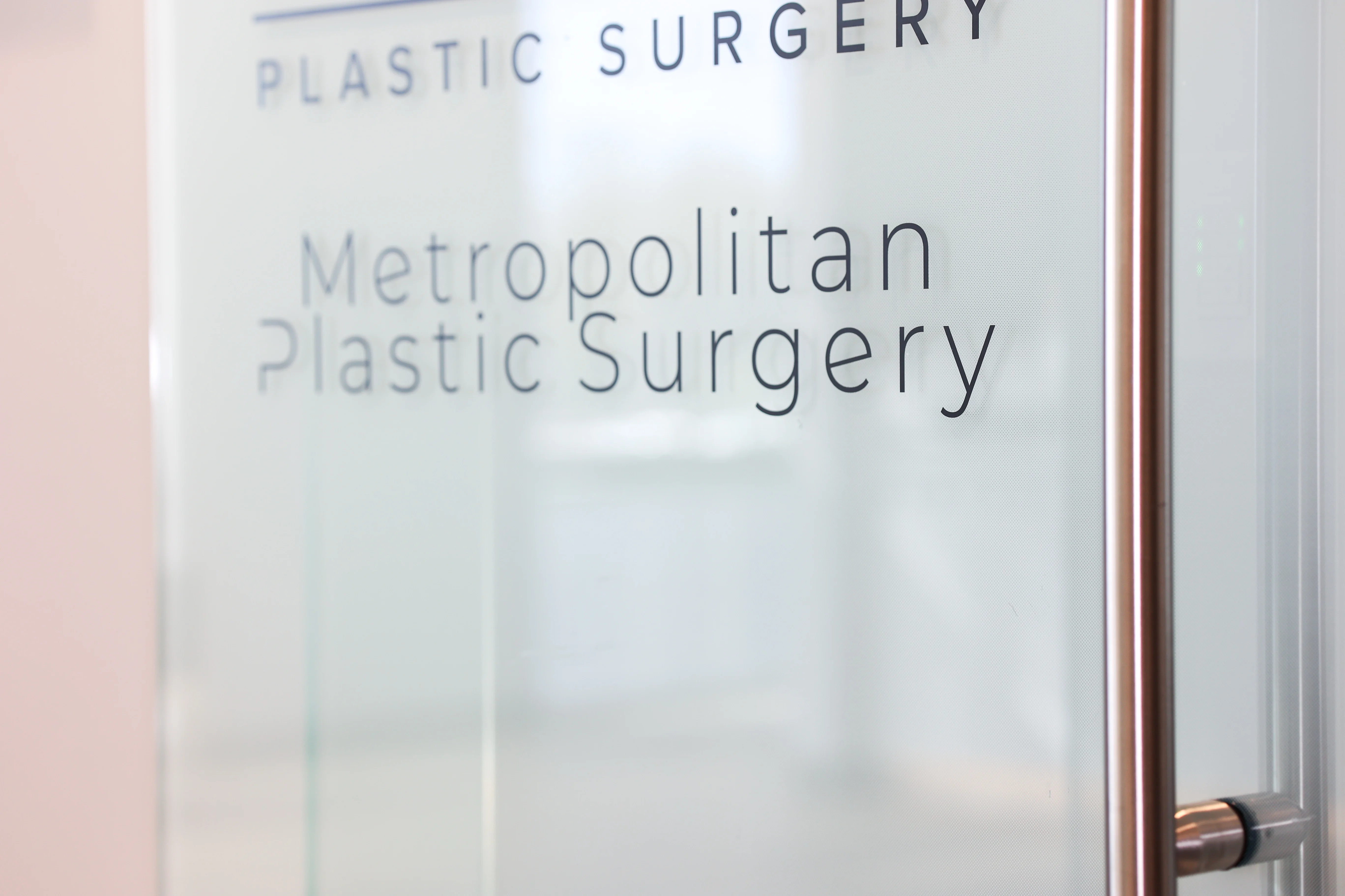 Close-up of Metropolitan Plastic Surgery name etched on glass office door in Scottsdale, Arizona, conveying modern professional branding.
