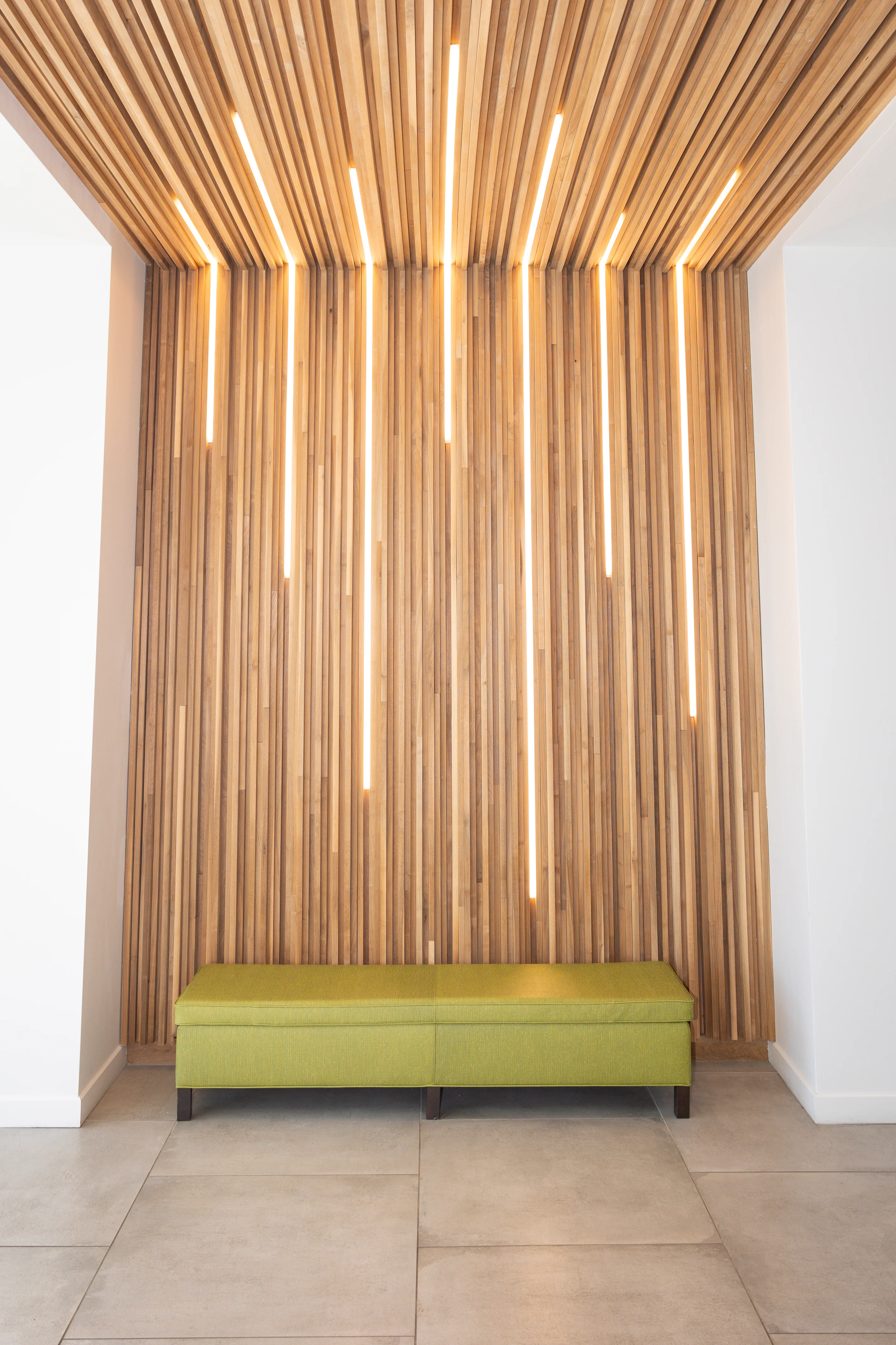 Architectural wood slat feature wall with integrated lighting and lime green bench in Metropolitan Plastic Surgery’s Scottsdale reception area.