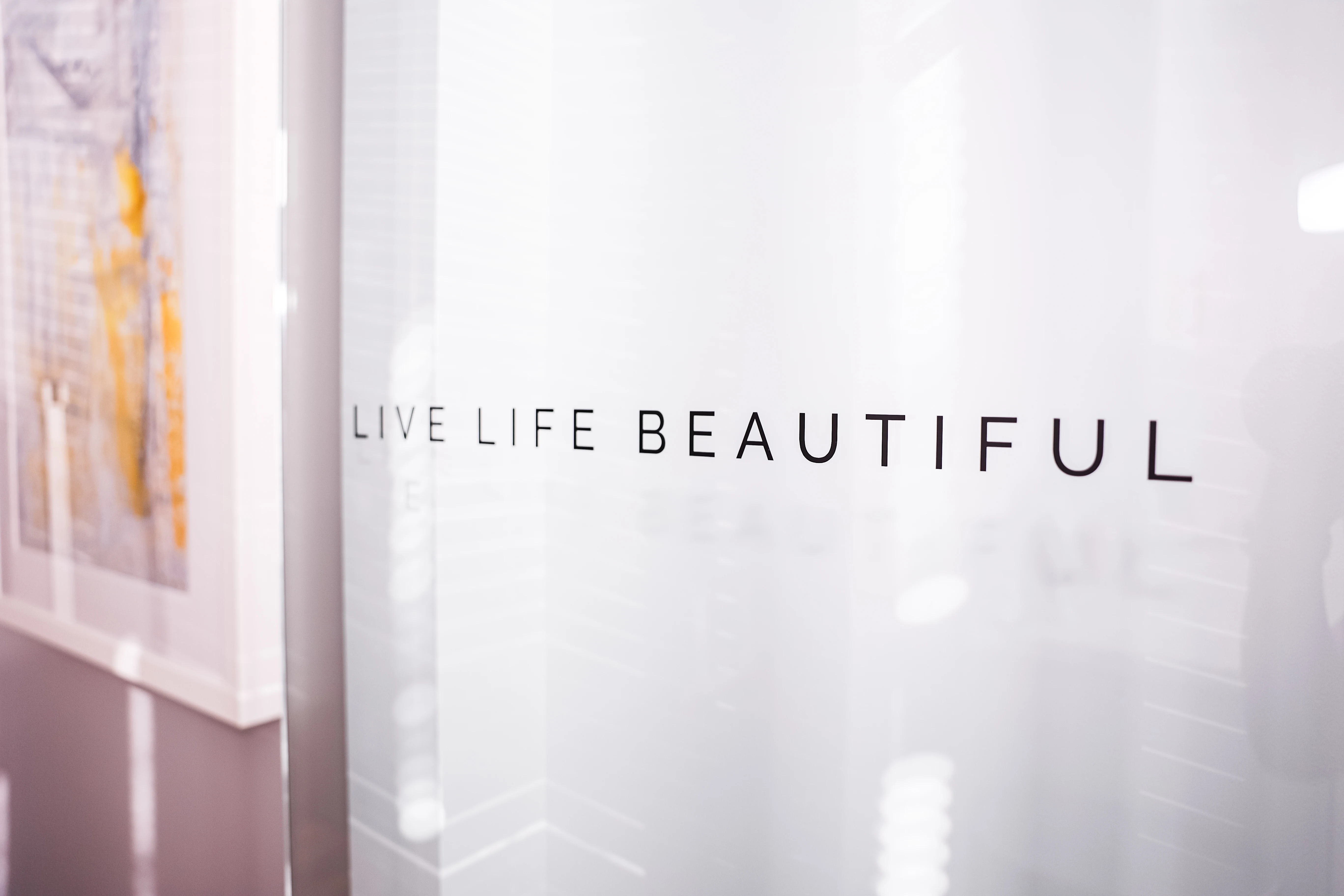 ‘LIVE LIFE BEAUTIFUL’ motto on frosted glass office partition in Metropolitan Plastic Surgery’s Scottsdale location, with bright modern interior.