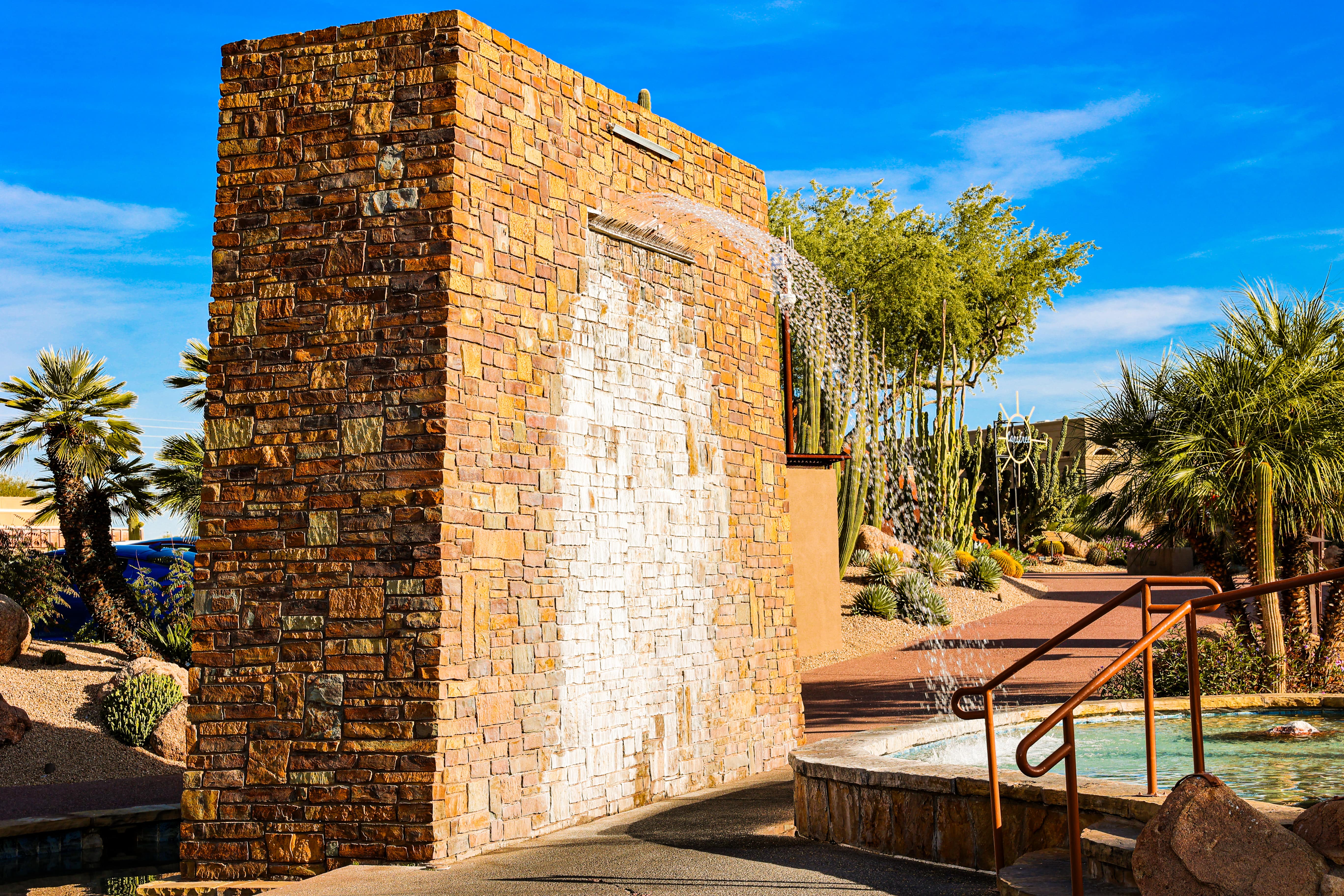 Outdoor water feature with stacked stone wall and cascading fountain in Carefree, AZ, with desert landscaping of palms and cacti.