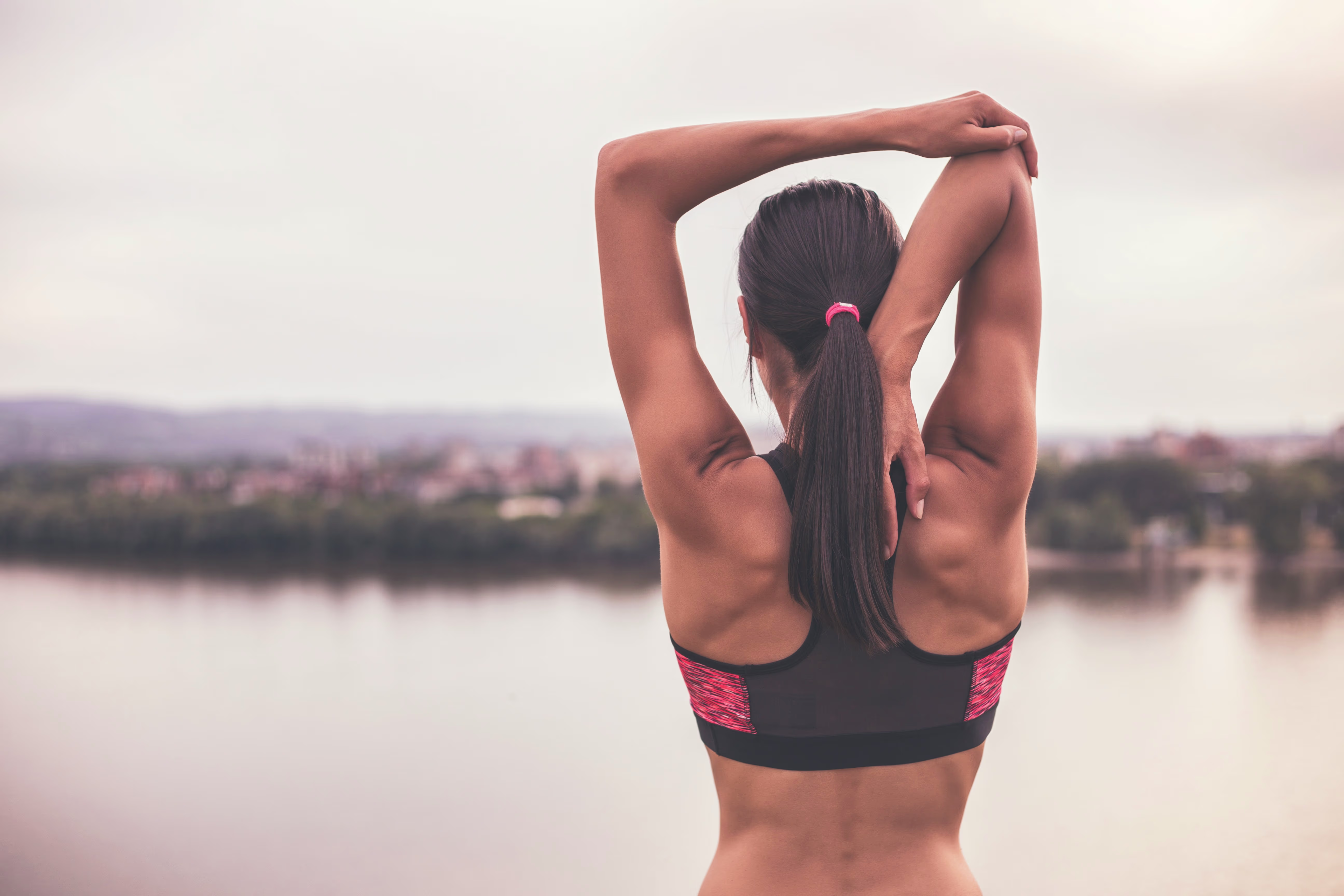 Athletic woman stretching arms outdoors, showing toned upper arms after arm lift surgery (brachioplasty).