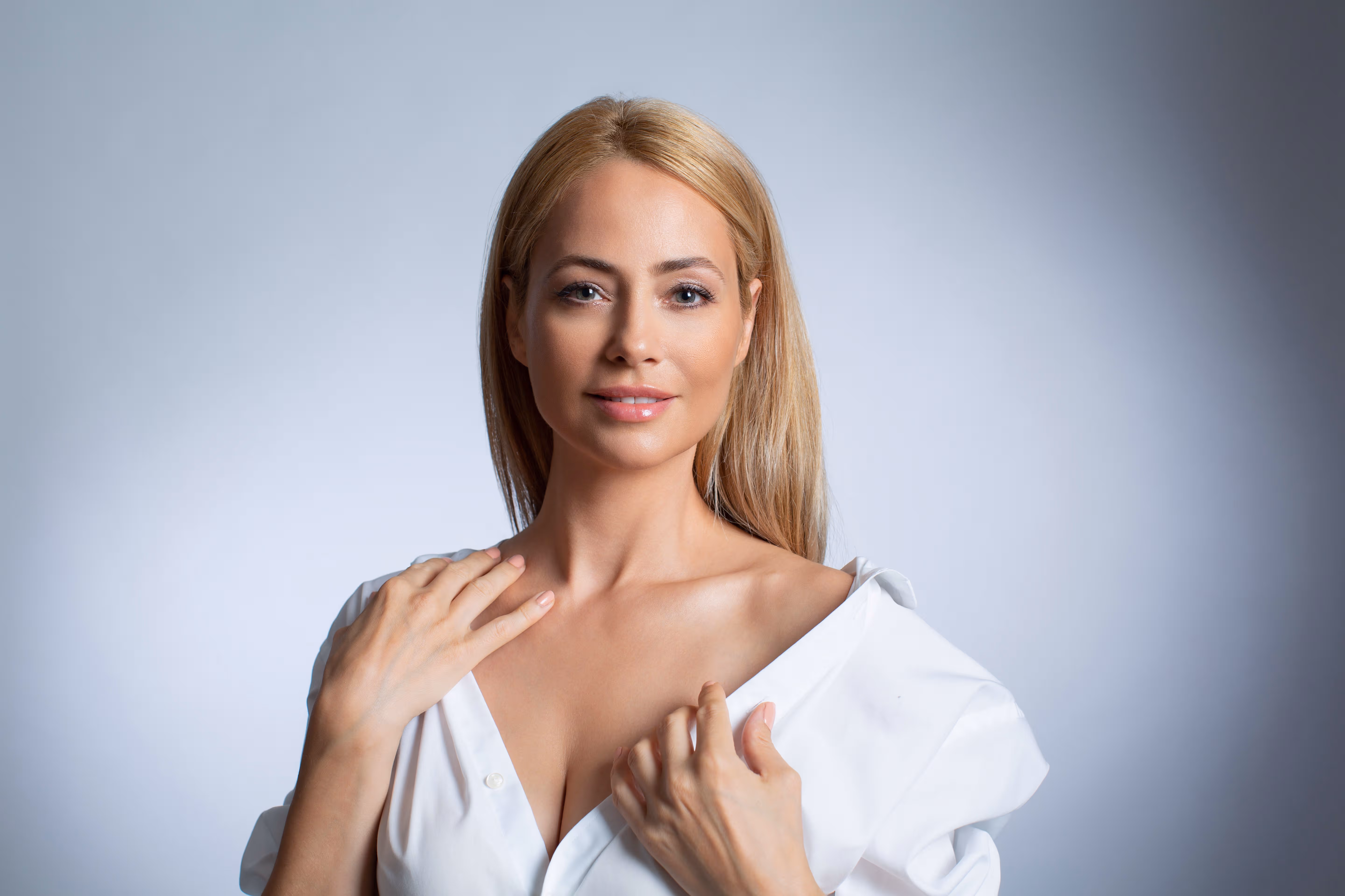 Confident woman with large natural breasts smiling and standing in a relaxed pose, representing empowerment and optimism before undergoing breast reduction surgery.