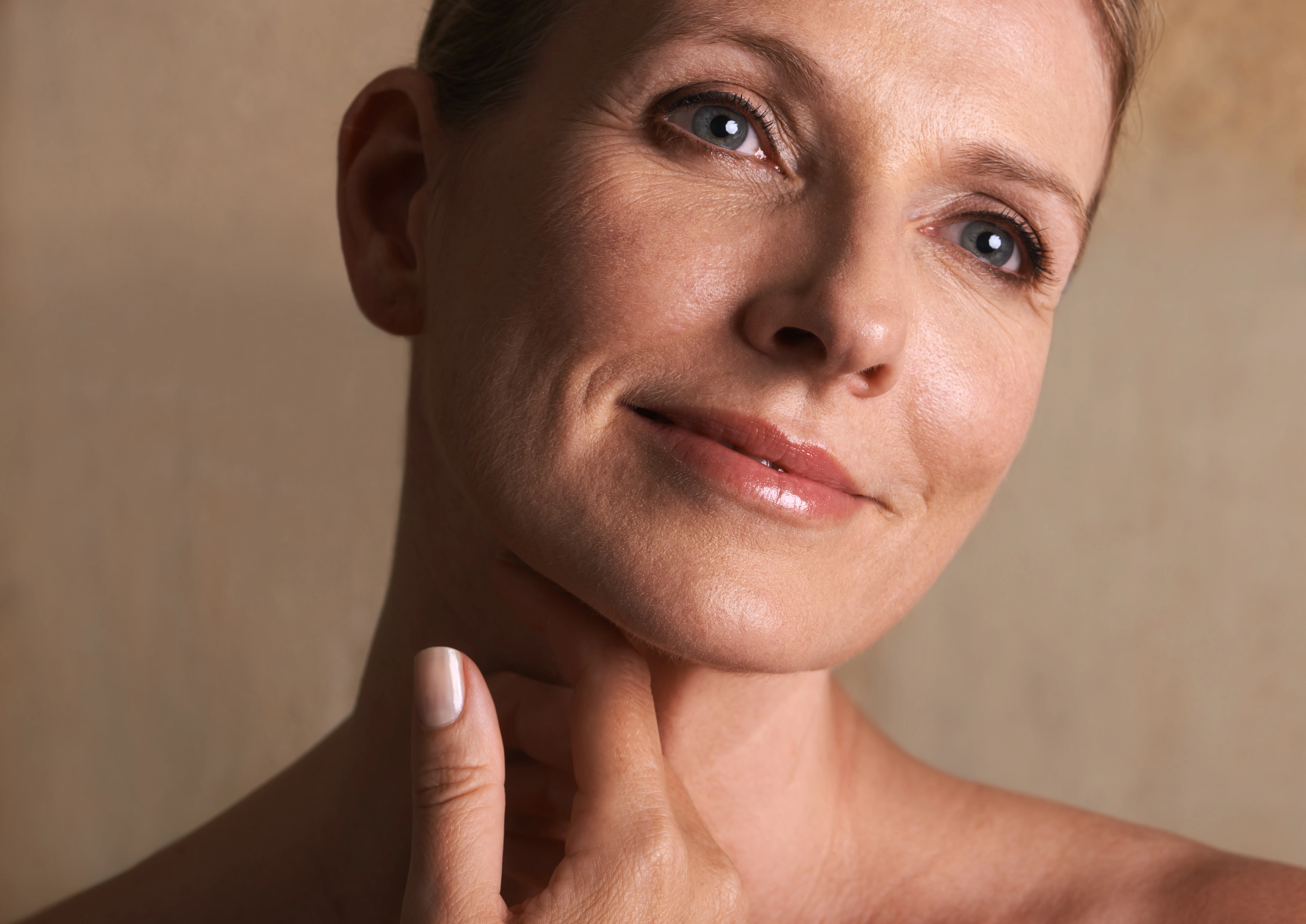 Close-up of a mature woman smiling gently, showing refreshed eyes and lifted brows after eyelid and brow surgery.