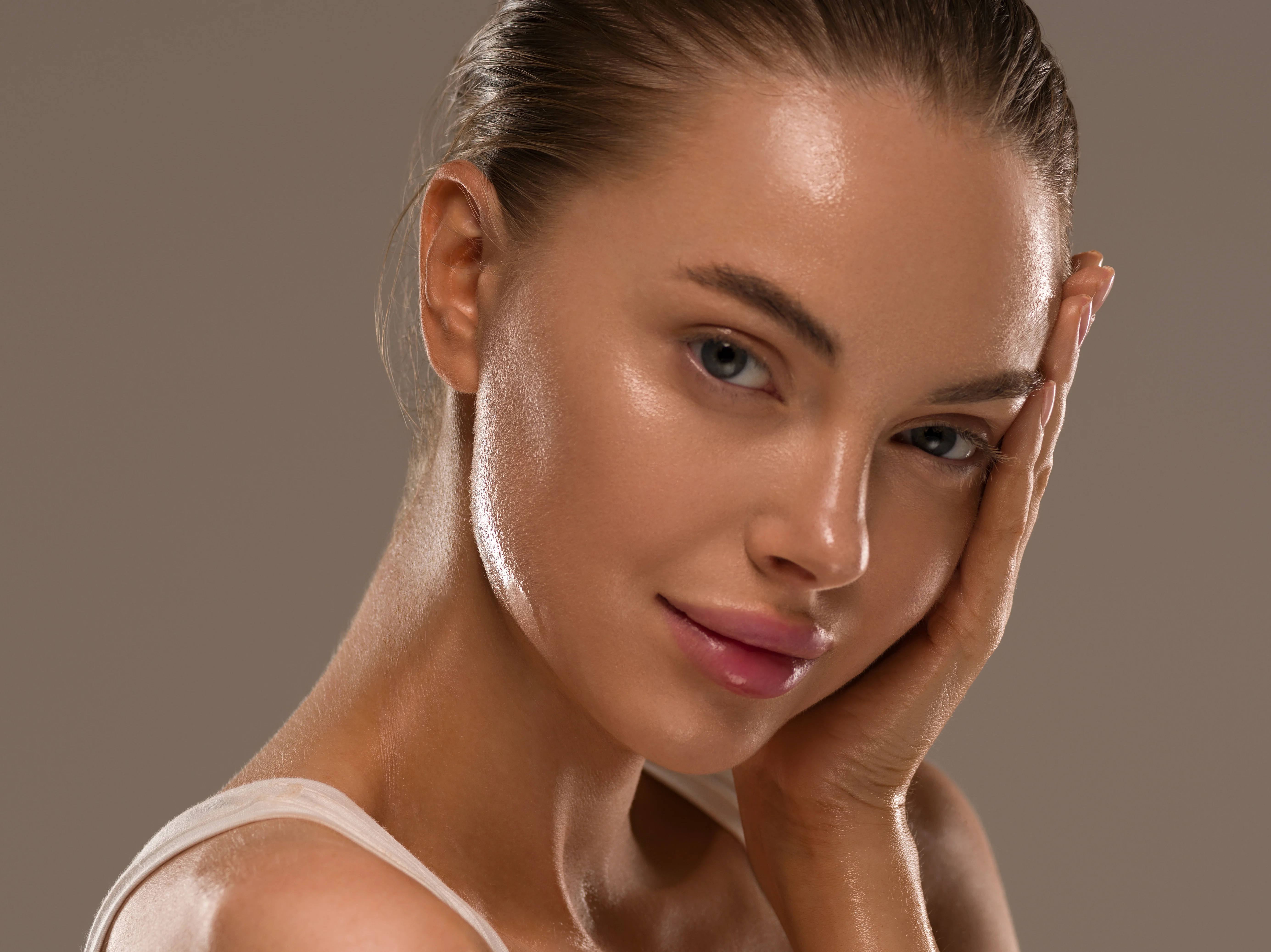 Woman with radiant skin and a defined chin gently resting her hand on her face, showcasing natural-looking results of neck and chin liposuction.