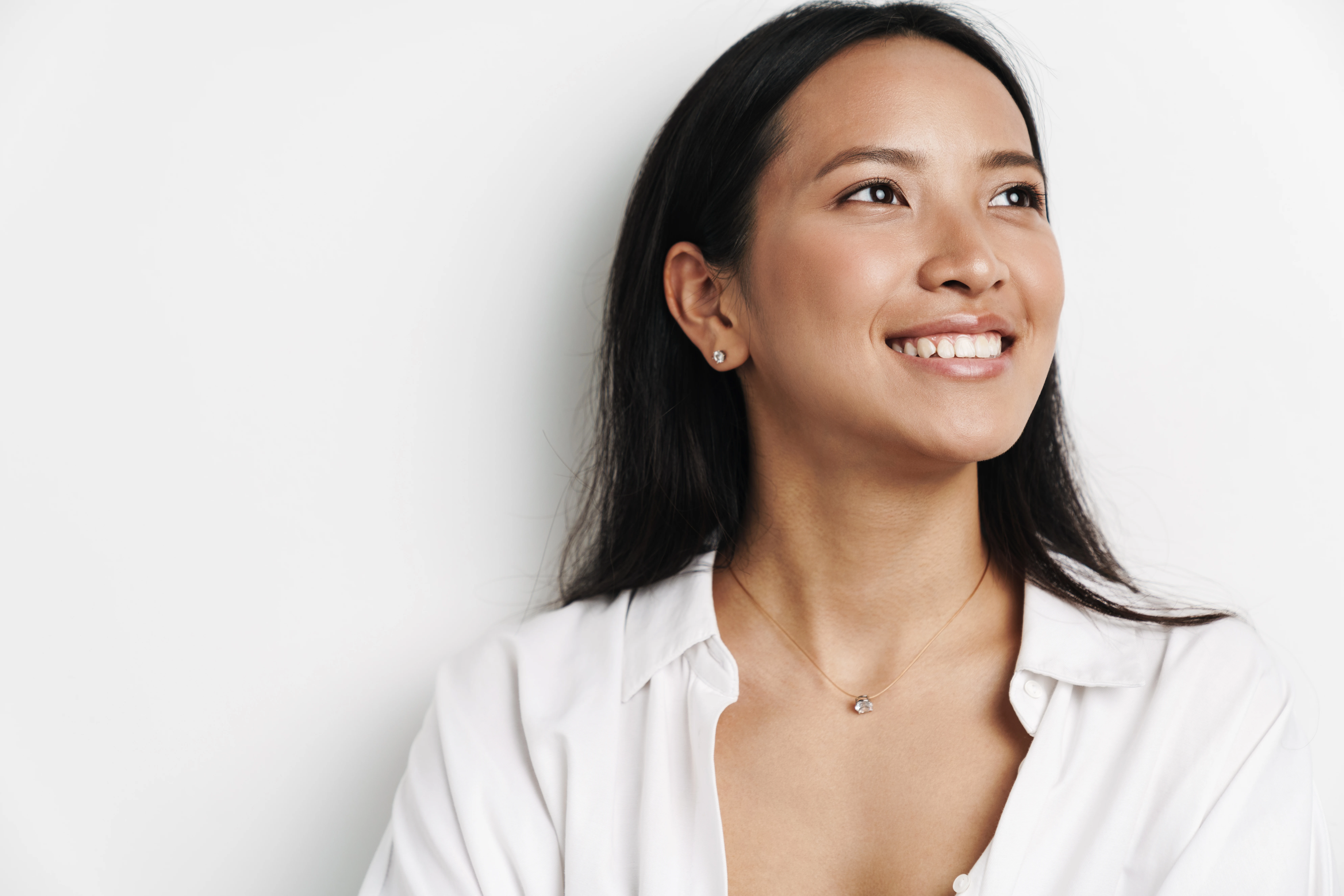 Woman smiling confidently with hair tucked behind her ear, showing natural ear shape and projection after ear pinning surgery.