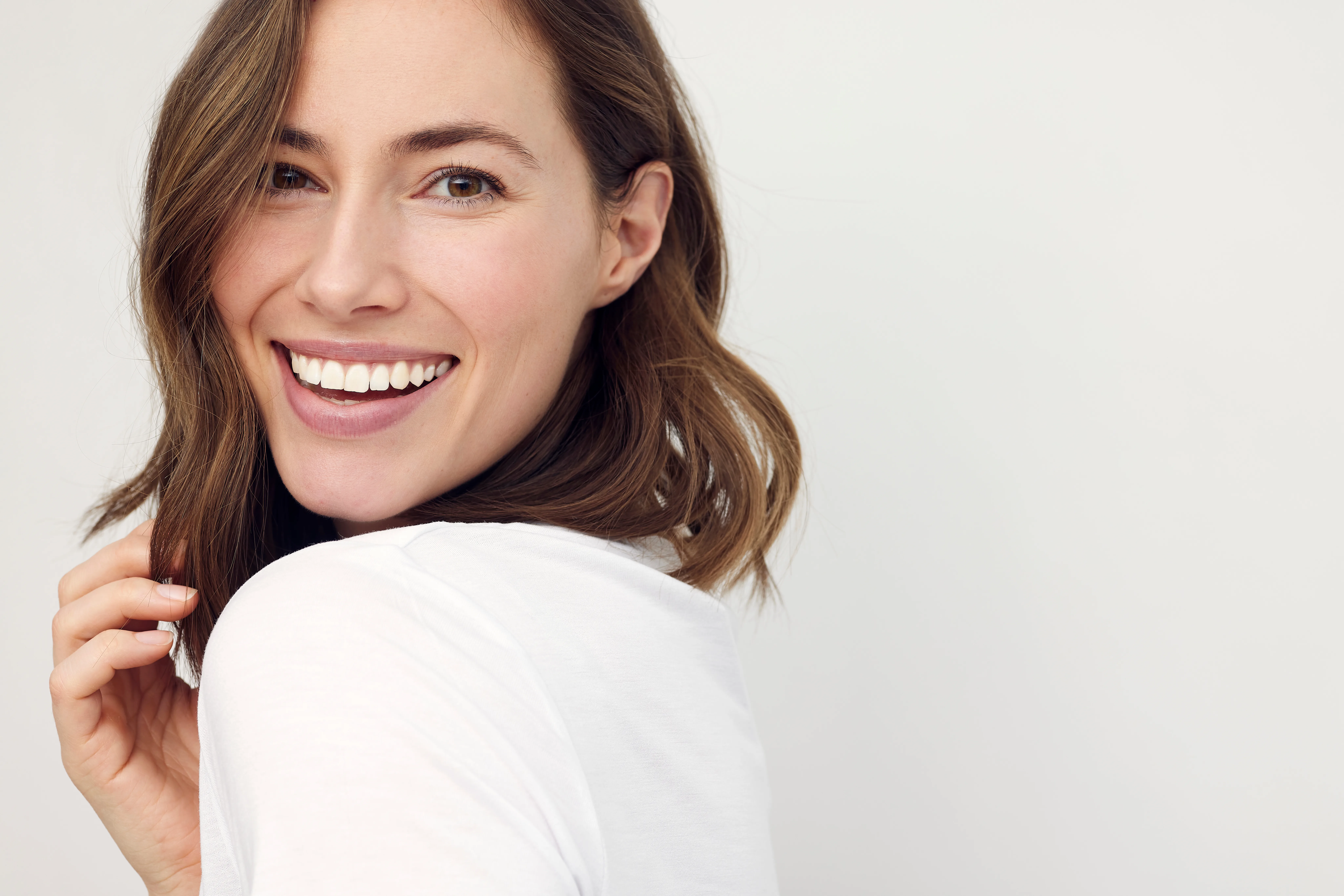 Woman smiling confidently with radiant, youthful skin and balanced facial features, showcasing natural-looking dermal filler results.