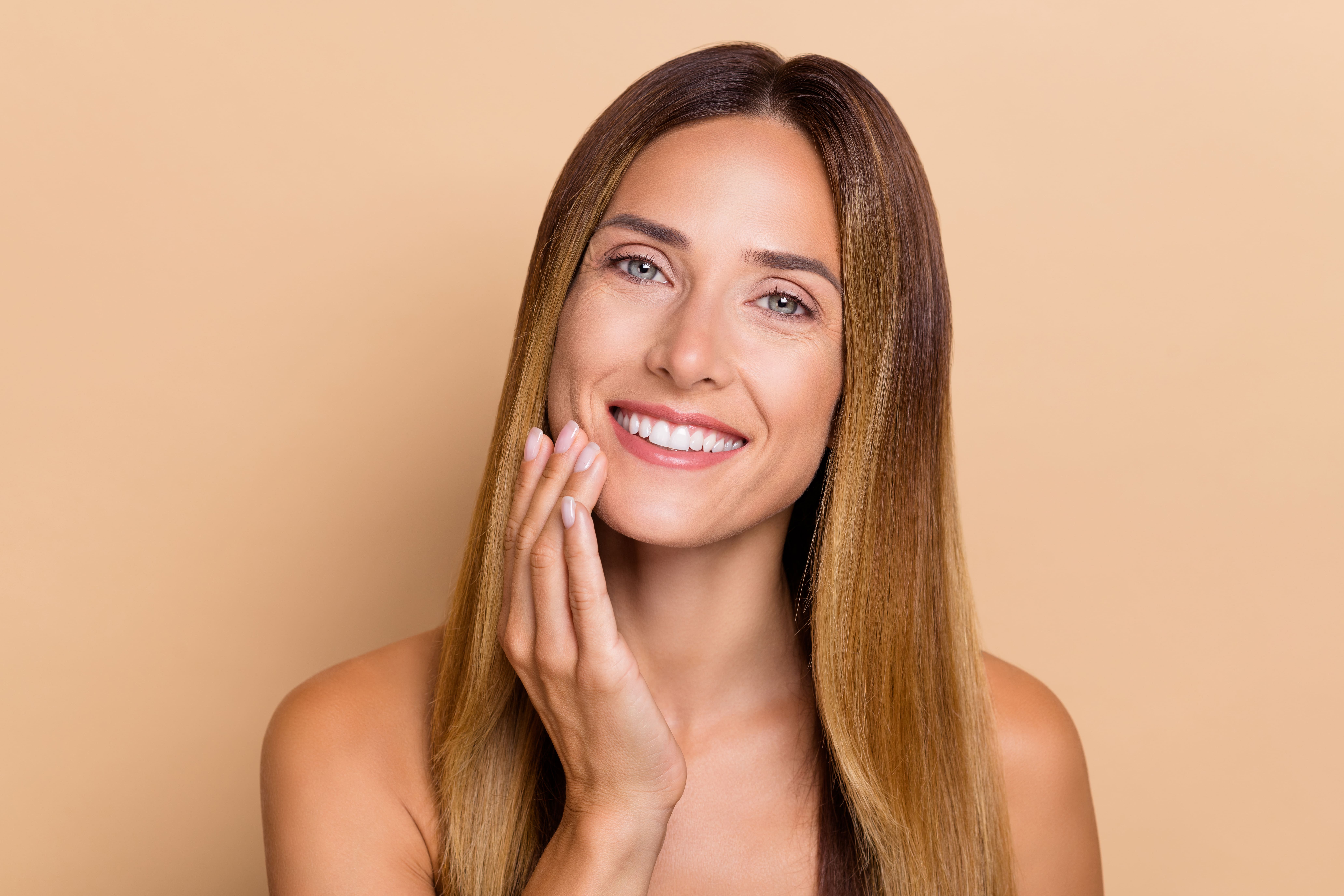 Smiling woman gently touching her cheek, showcasing radiant and smooth skin after PRP or exosome facial therapy
