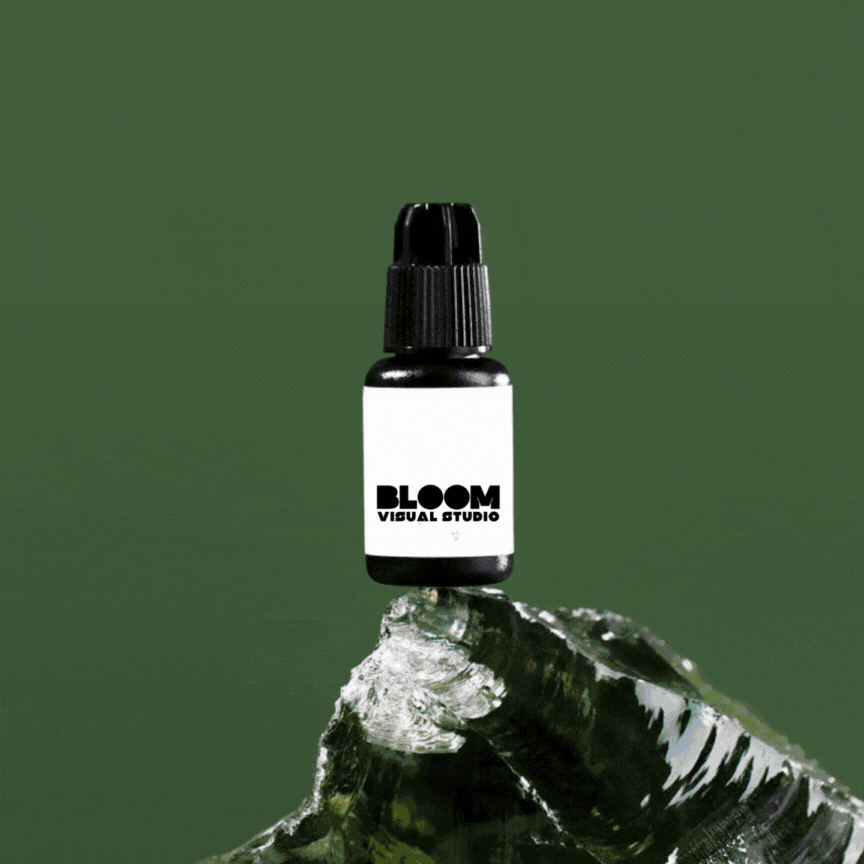 Bottiglia nera con etichetta bianca e scritta Bloom Visual Studio su un pezzo di vetro riflettente su sfondo verde.