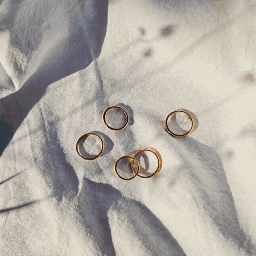 Cinque anelli dorati posati su un tessuto bianco spiegazzato con ombre soffuse.