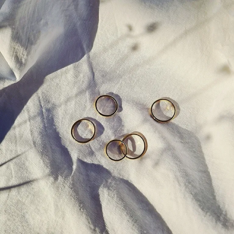 Cinque fedi nuziali d'oro sparse su tessuto bianco con ombre morbide.