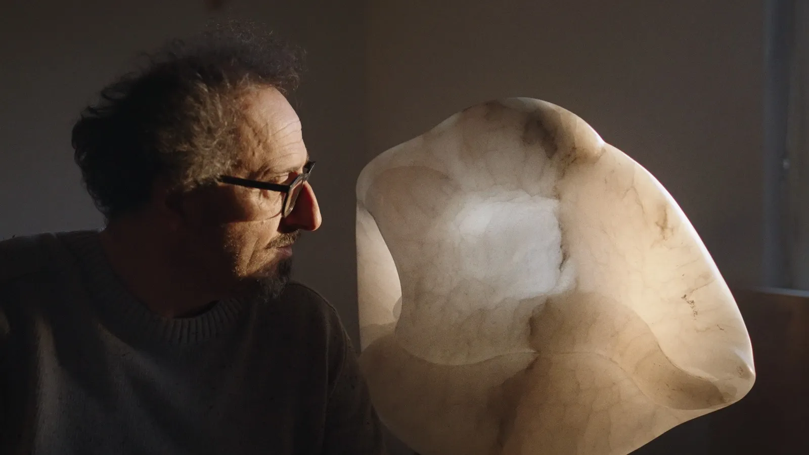 Scultore con occhiali guarda attentamente una scultura in marmo chiara e levigata.